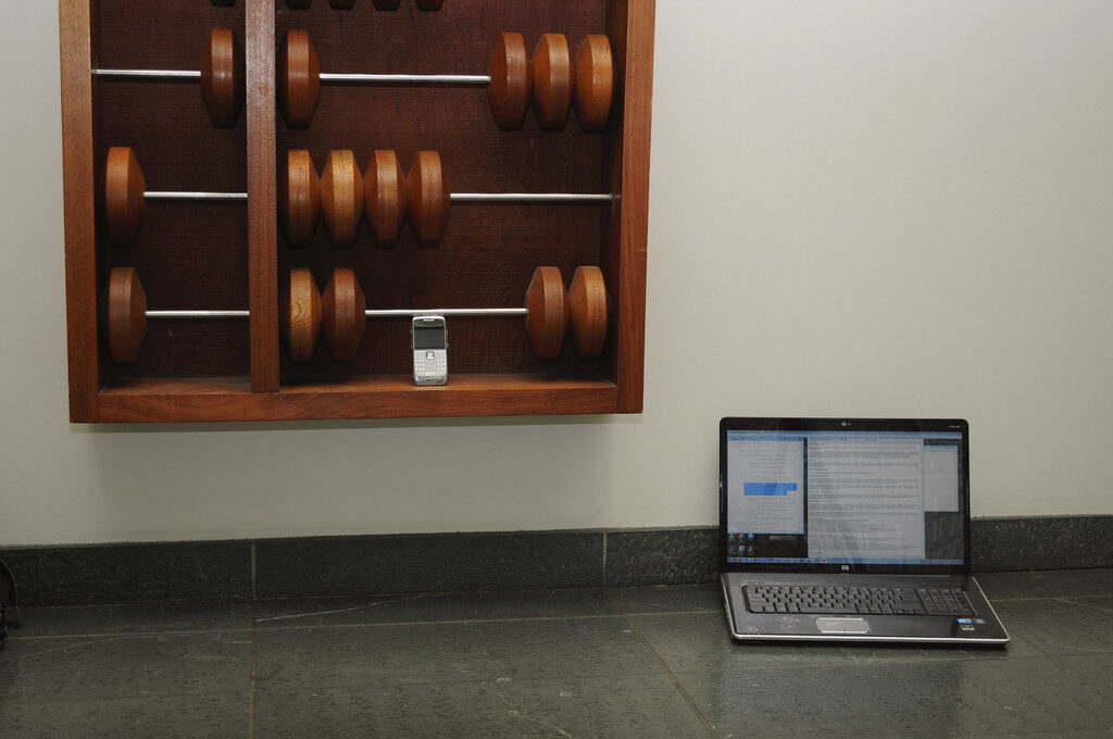 Großer Holz-Abakus an einer Wand, davor ein aufgeklappter Laptop auf dem Boden
